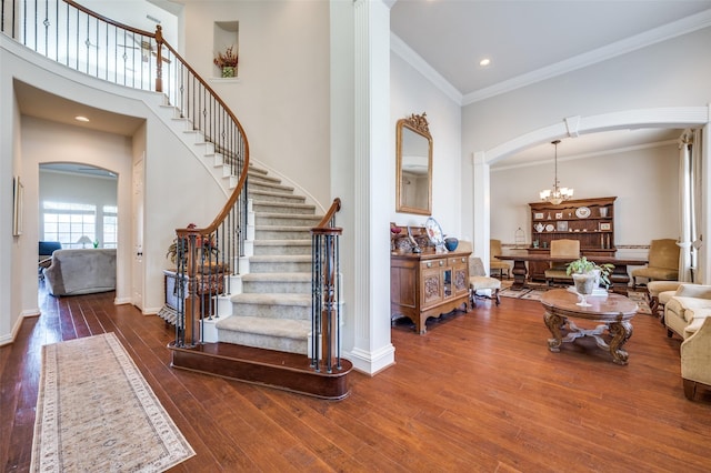 foyer with a high ceiling, ornamental molding, dark wood-type flooring, and an inviting chandelier