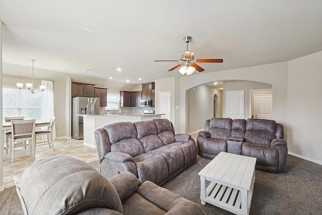 living area featuring arched walkways, a healthy amount of sunlight, baseboards, and ceiling fan with notable chandelier