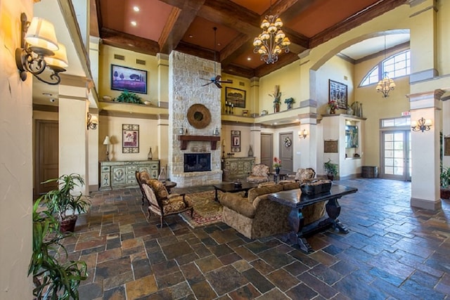 living area with coffered ceiling, a towering ceiling, stone tile flooring, a stone fireplace, and beam ceiling