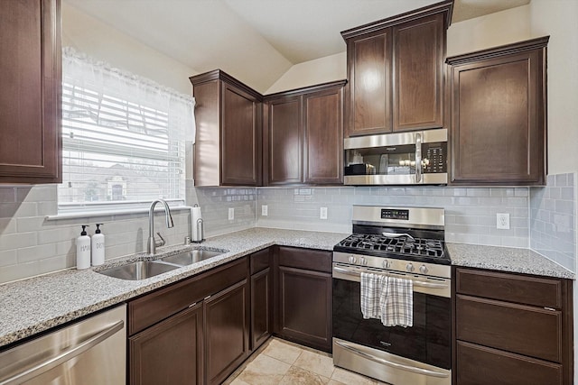 kitchen with light stone counters, a sink, vaulted ceiling, stainless steel appliances, and backsplash