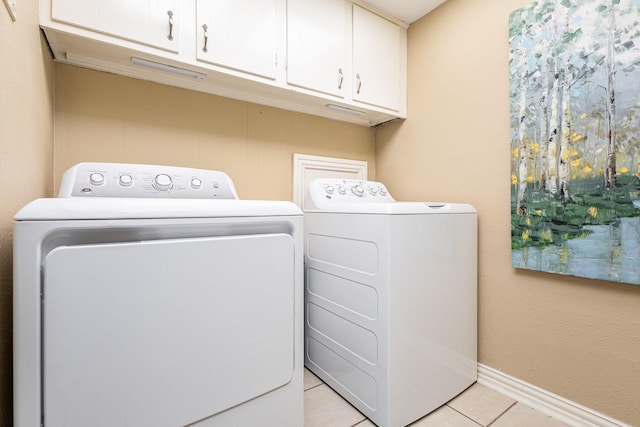 clothes washing area featuring washer and dryer, light tile patterned floors, and cabinets