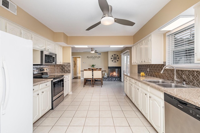 kitchen featuring light tile patterned flooring, sink, white cabinetry, a multi sided fireplace, and stainless steel appliances