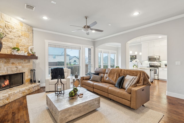 living room featuring crown molding, a stone fireplace, ceiling fan, and light wood-type flooring