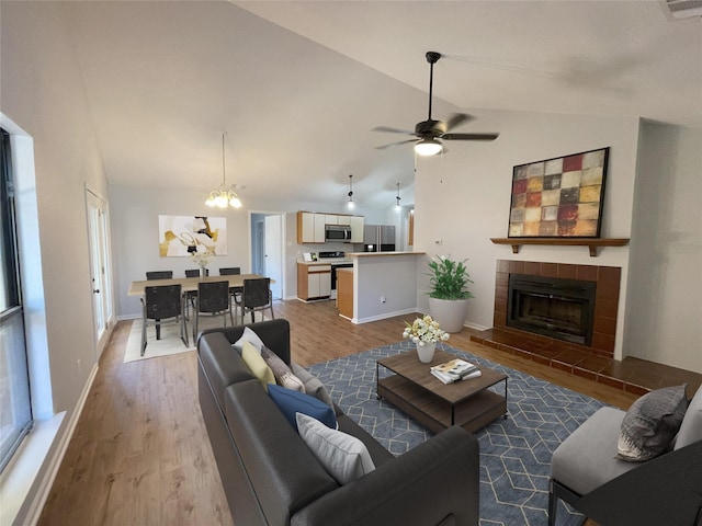 living room with a tiled fireplace, high vaulted ceiling, ceiling fan with notable chandelier, and light hardwood / wood-style floors