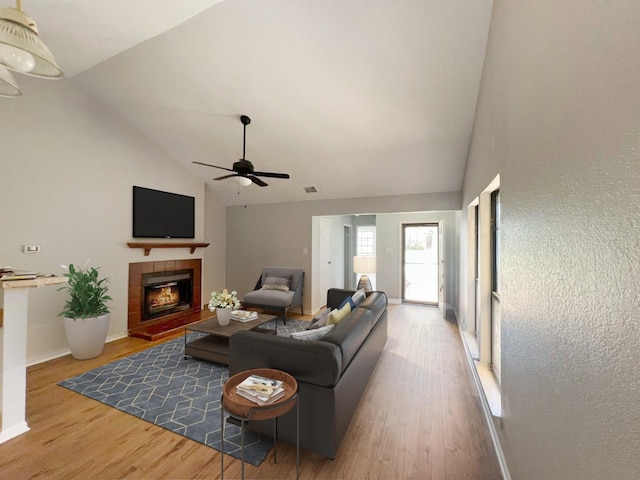 living room featuring hardwood / wood-style flooring, ceiling fan, high vaulted ceiling, and a tile fireplace