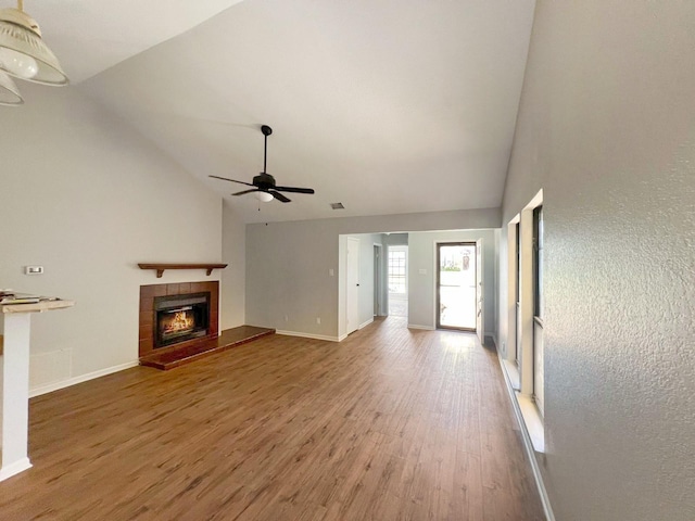 unfurnished living room featuring a tile fireplace, high vaulted ceiling, hardwood / wood-style floors, and ceiling fan