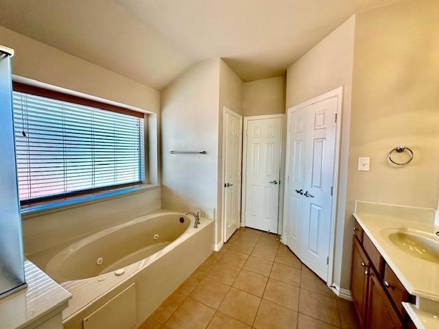 bathroom with lofted ceiling, vanity, tile patterned flooring, and a tub