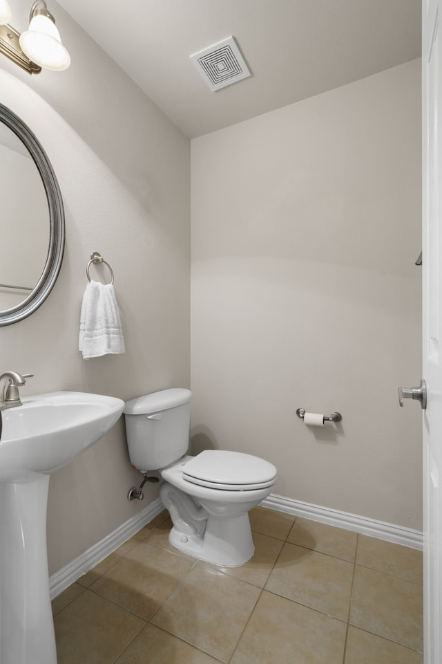 half bath with tile patterned floors, visible vents, toilet, a sink, and baseboards