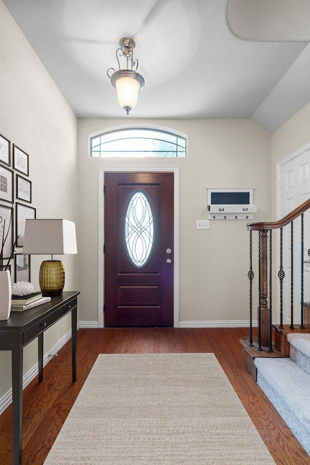 foyer with stairs, vaulted ceiling, wood finished floors, and baseboards