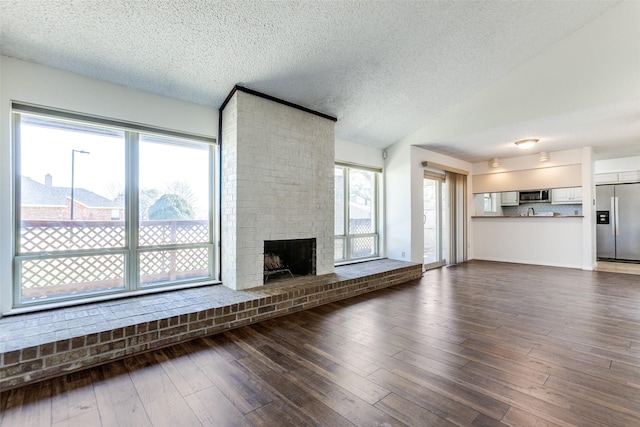 unfurnished living room featuring lofted ceiling, dark wood-type flooring, a textured ceiling, and a brick fireplace