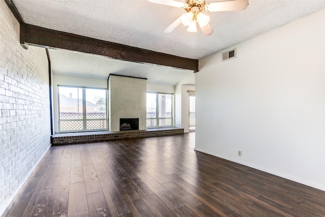 unfurnished living room with brick wall, dark hardwood / wood-style floors, a brick fireplace, a textured ceiling, and beam ceiling