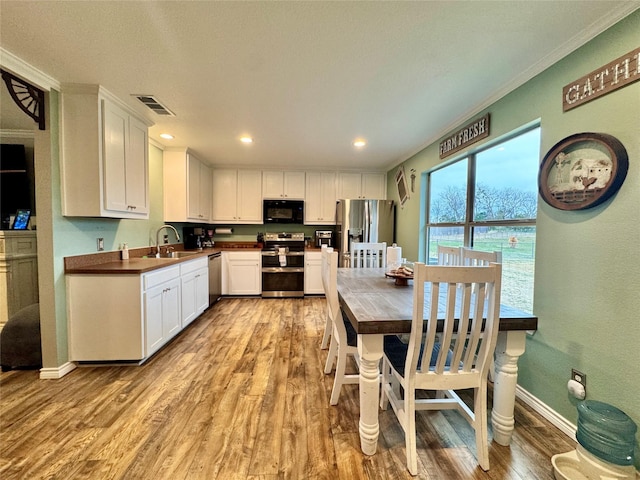 kitchen with sink, white cabinetry, light wood-type flooring, ornamental molding, and appliances with stainless steel finishes