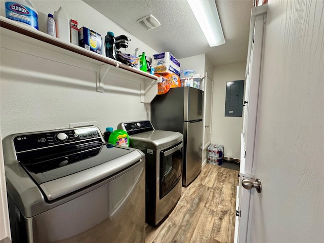 clothes washing area featuring electric panel, washer and dryer, a textured ceiling, and light wood-type flooring