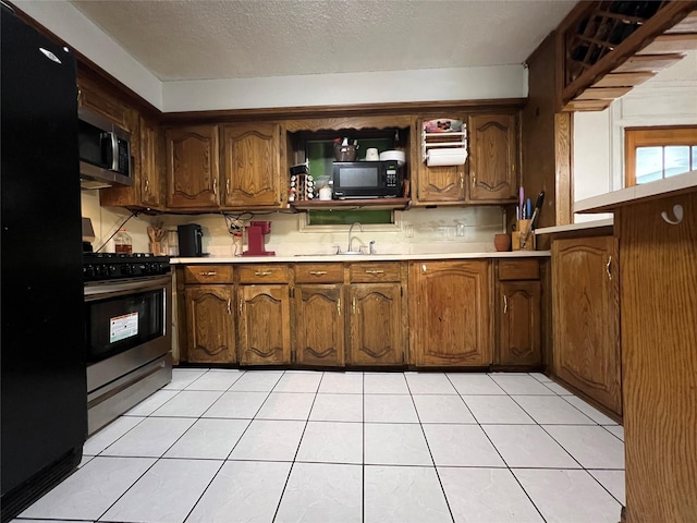 kitchen with sink, light tile patterned floors, black appliances, and a textured ceiling