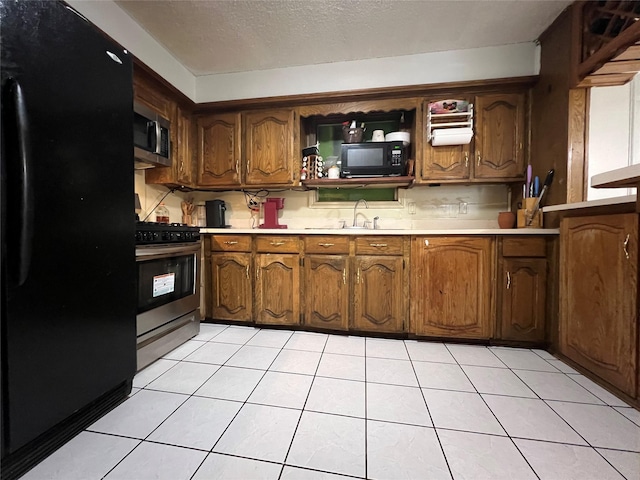 kitchen with light tile patterned floors, sink, a textured ceiling, and black appliances