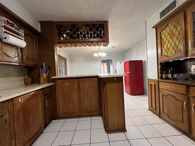 kitchen featuring light tile patterned floors, fridge, kitchen peninsula, and a textured ceiling