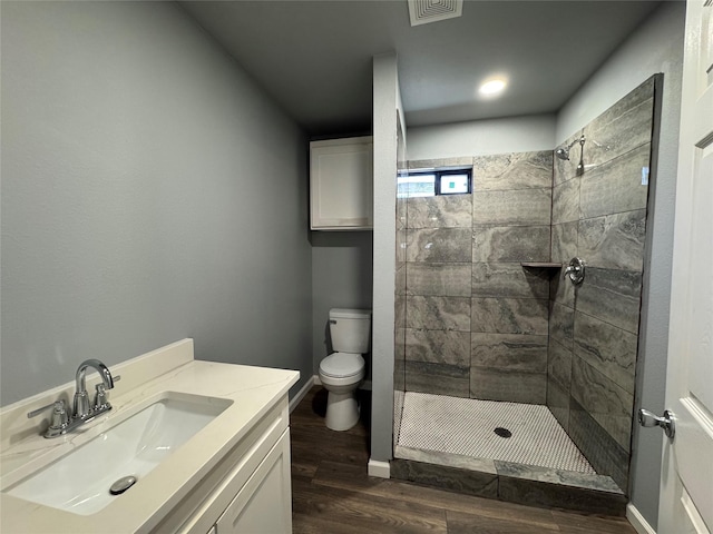 bathroom featuring vanity, wood-type flooring, a tile shower, and toilet