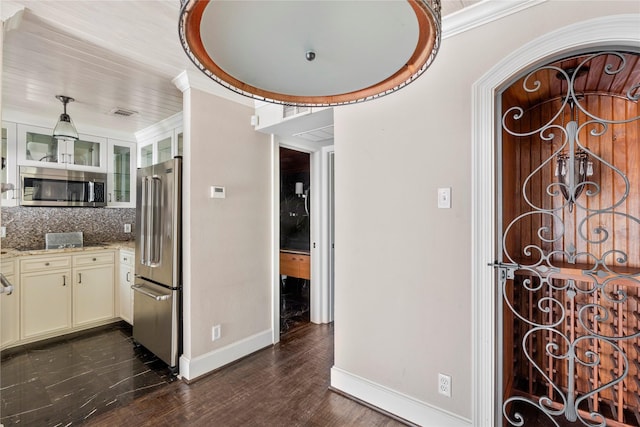 kitchen with dark wood-type flooring, light stone counters, backsplash, stainless steel appliances, and cream cabinetry