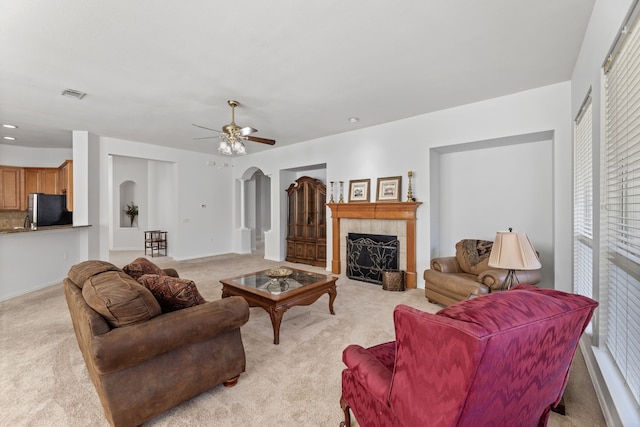 living room with ceiling fan, a tile fireplace, and light carpet