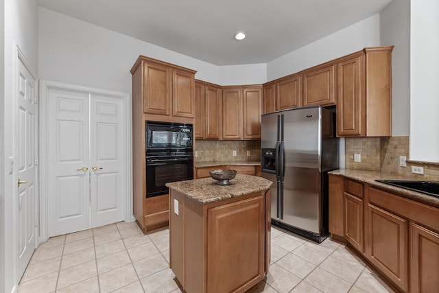 kitchen with light tile patterned flooring, a kitchen island, light stone counters, and black appliances