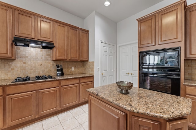 kitchen featuring light stone counters, gas cooktop, black microwave, and a center island