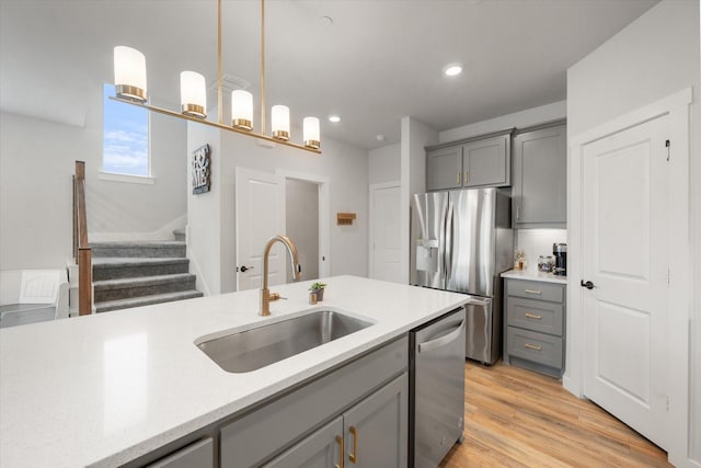 kitchen with sink, light hardwood / wood-style flooring, gray cabinets, appliances with stainless steel finishes, and hanging light fixtures