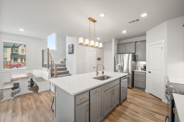 kitchen featuring gray cabinets, pendant lighting, sink, stainless steel appliances, and a center island with sink