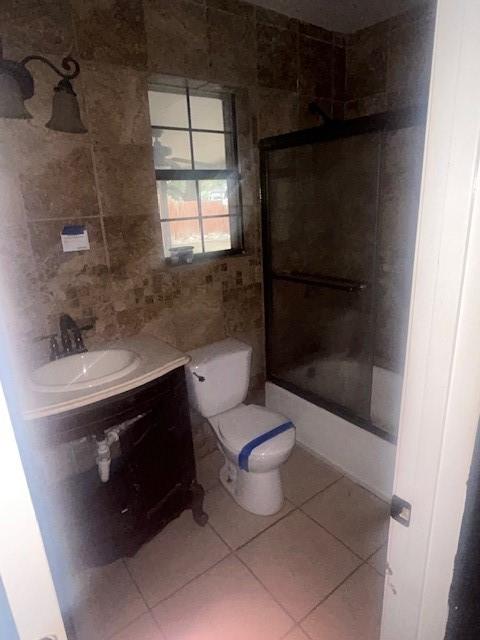 full bathroom with sink, tile walls, shower / bath combination with glass door, toilet, and tile patterned floors