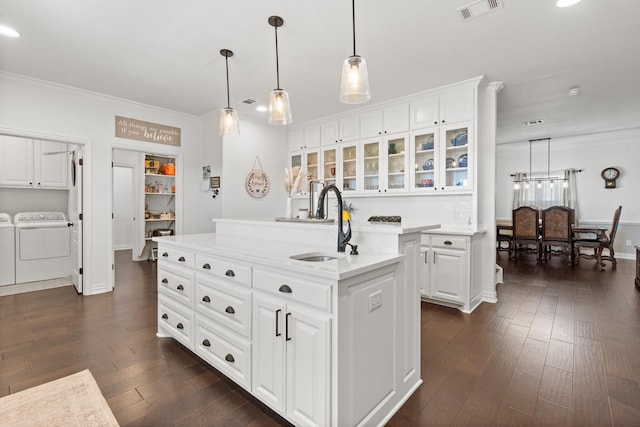 kitchen featuring decorative light fixtures, an island with sink, sink, white cabinets, and washing machine and clothes dryer