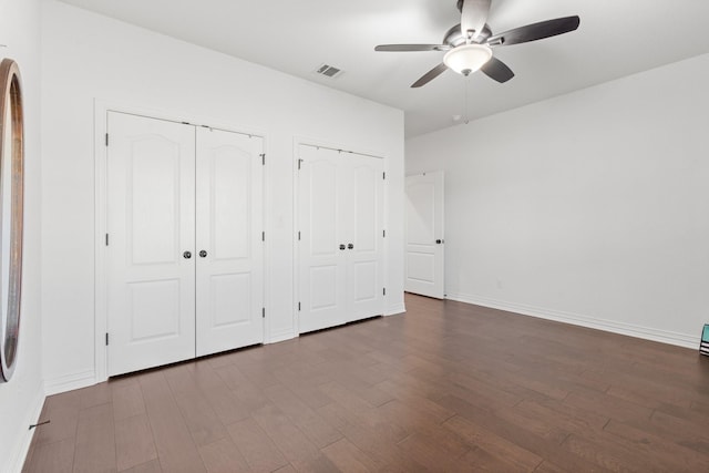 unfurnished bedroom with ceiling fan, hardwood / wood-style floors, and two closets