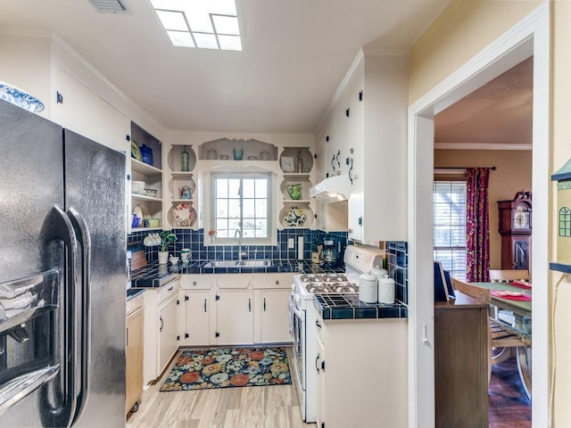 kitchen featuring gas range gas stove, black fridge, white cabinetry, crown molding, and tile countertops