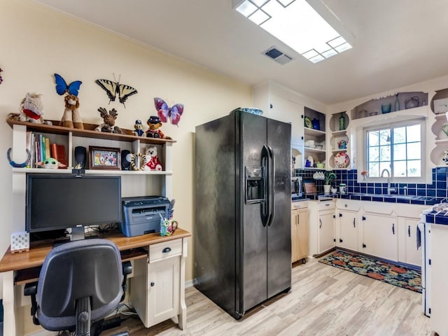 kitchen with black fridge, sink, white cabinets, and light wood-type flooring