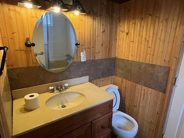 bathroom featuring vanity, toilet, tile walls, and wood walls