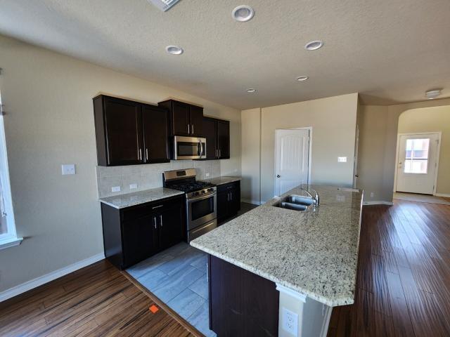 kitchen featuring sink, stainless steel appliances, light stone countertops, a center island with sink, and dark hardwood / wood-style flooring