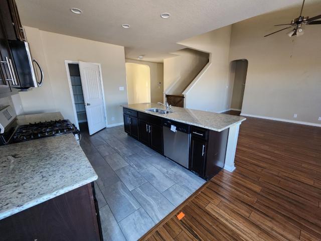 kitchen with dark hardwood / wood-style flooring, a kitchen island with sink, ceiling fan, light stone counters, and stainless steel appliances