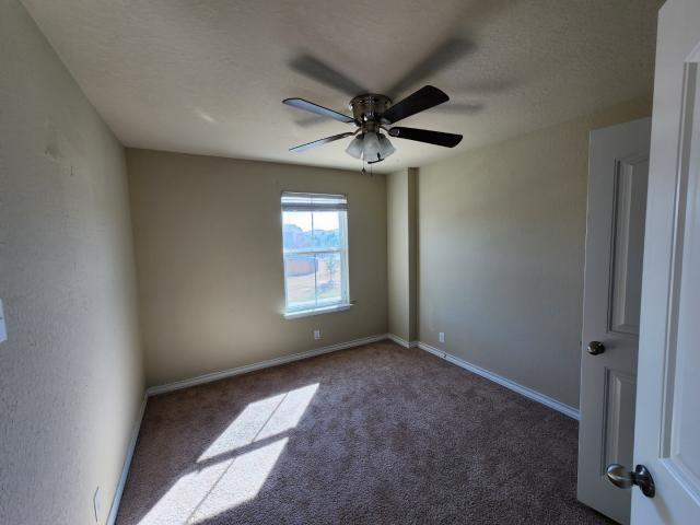 spare room featuring ceiling fan, dark carpet, and a textured ceiling