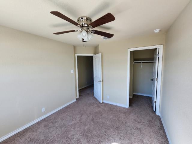 unfurnished bedroom featuring light carpet, a walk in closet, a closet, and ceiling fan