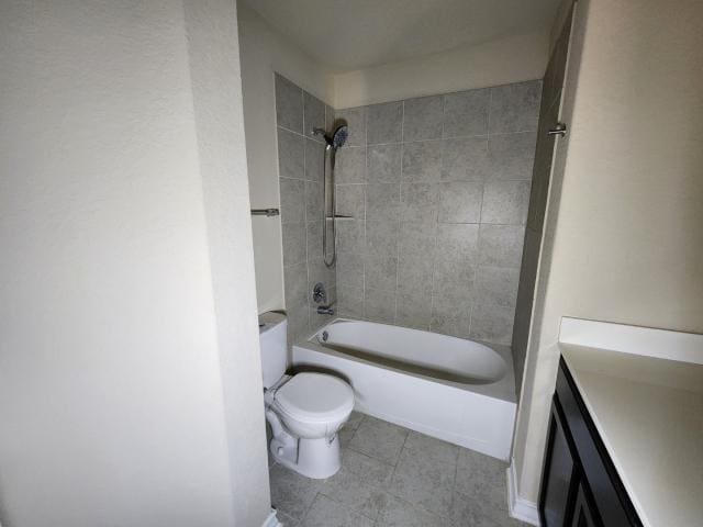 full bathroom with tile patterned flooring, tiled shower / bath, vanity, and toilet