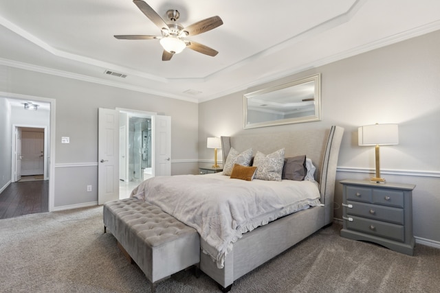 bedroom with crown molding, connected bathroom, a tray ceiling, and dark carpet