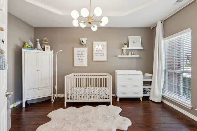 bedroom featuring a tray ceiling, dark hardwood / wood-style floors, and a nursery area