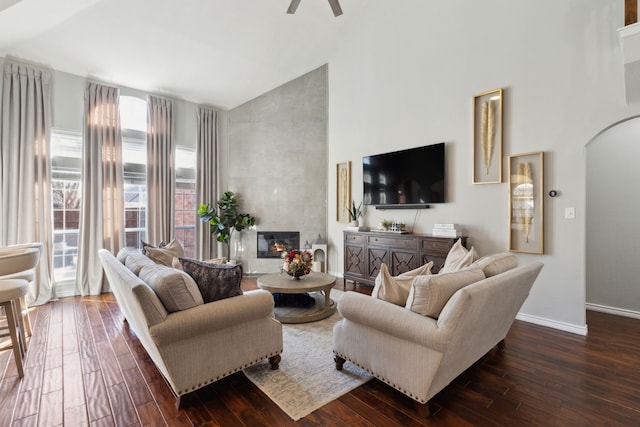 living room featuring dark wood-type flooring, ceiling fan, a fireplace, and high vaulted ceiling