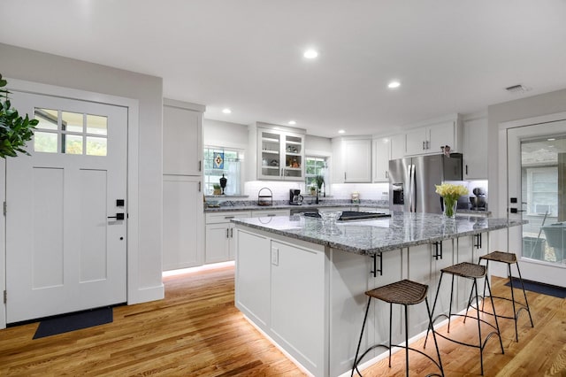 kitchen featuring white cabinetry, a center island, stainless steel fridge with ice dispenser, light stone countertops, and light hardwood / wood-style flooring