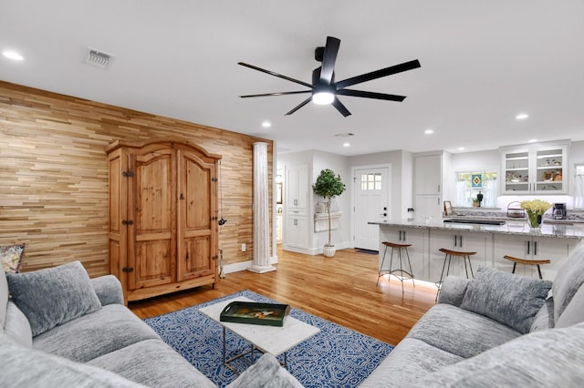 living room featuring ceiling fan, wood walls, and light wood-type flooring