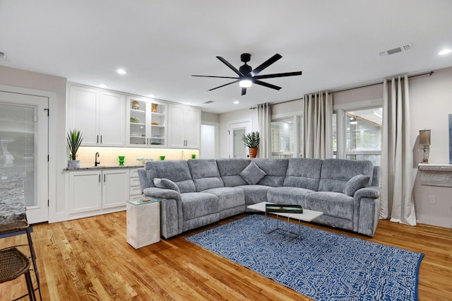 living room featuring wet bar, light hardwood / wood-style floors, and ceiling fan