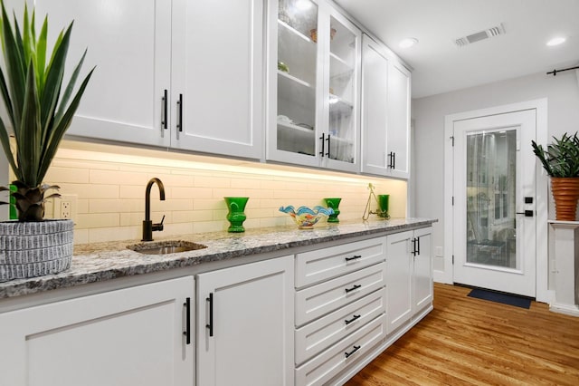 bar featuring sink, white cabinetry, light stone countertops, light hardwood / wood-style floors, and backsplash