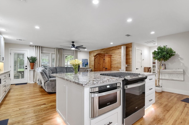 kitchen featuring light wood-type flooring, appliances with stainless steel finishes, an island with sink, light stone countertops, and white cabinets