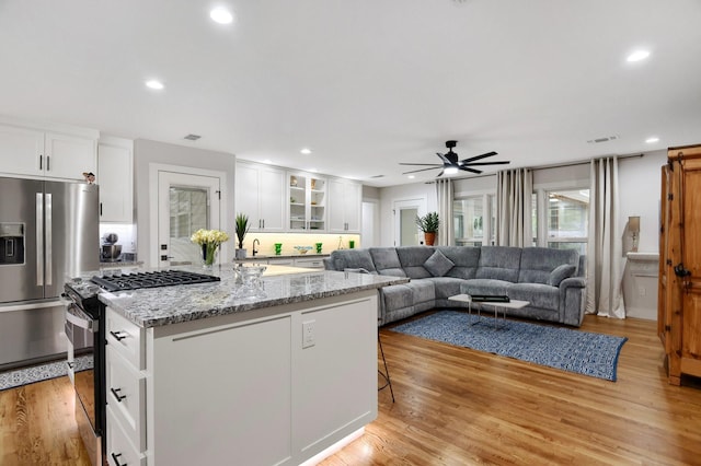 kitchen with white cabinetry, a kitchen island with sink, range with gas stovetop, and stainless steel fridge with ice dispenser