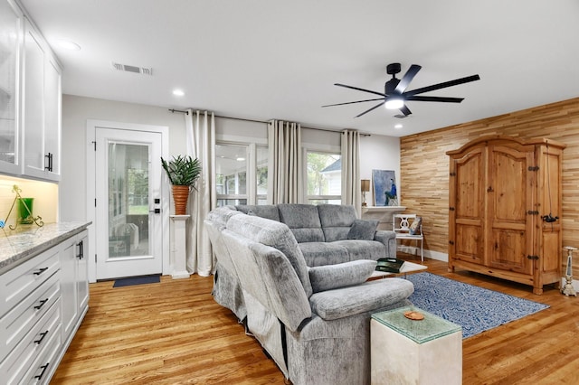 living room featuring light hardwood / wood-style floors, ceiling fan, and wood walls