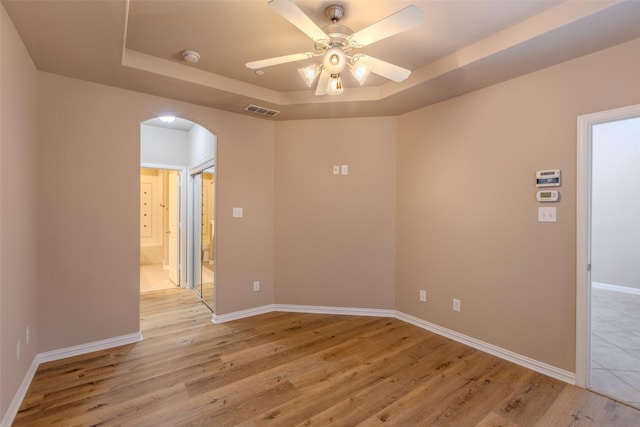 empty room with a raised ceiling, ceiling fan, and light hardwood / wood-style floors