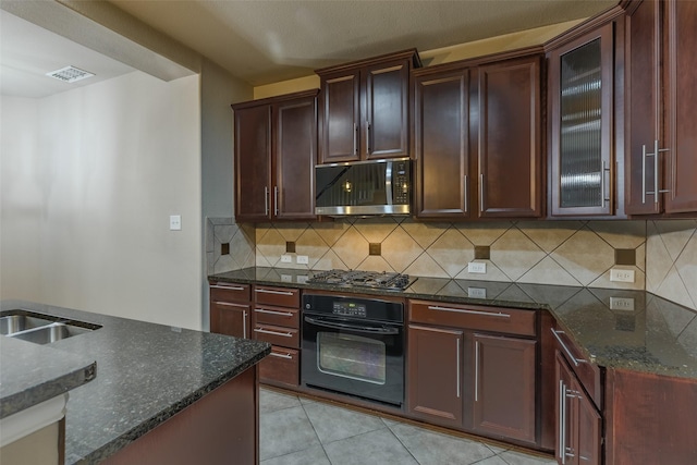 kitchen with backsplash, appliances with stainless steel finishes, light tile patterned floors, and dark stone counters